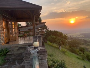 A stone staircase leading to a wooden deck with a view of a sunset over a hilly landscape. - Rift Valley Game Lodge (Rubirizi)