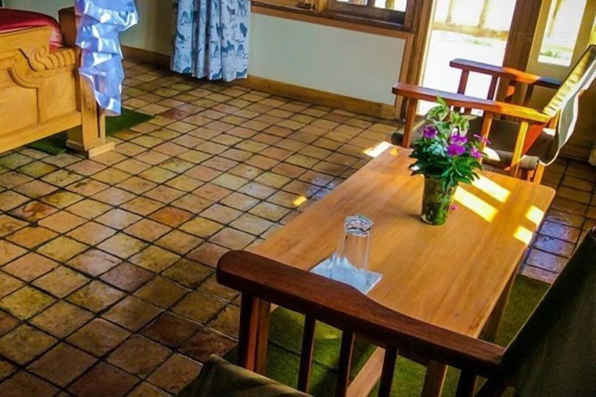Una habitación con un banco de madera, una mesa de madera con un florero y un suelo de baldosas.