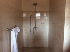 A shower with a handheld showerhead and a fixed overhead showerhead, a towel rack with a white towel, and tiled walls.