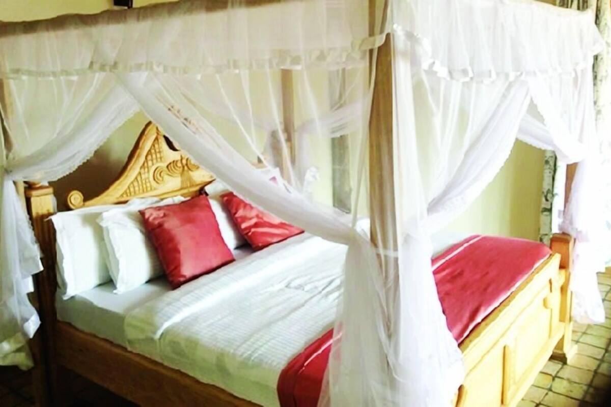 Una cama con dosel, almohadas y una manta roja.