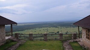 A stone building with a wooden fence overlooking a green valley. - Rift Valley Game Lodge (Rubirizi)