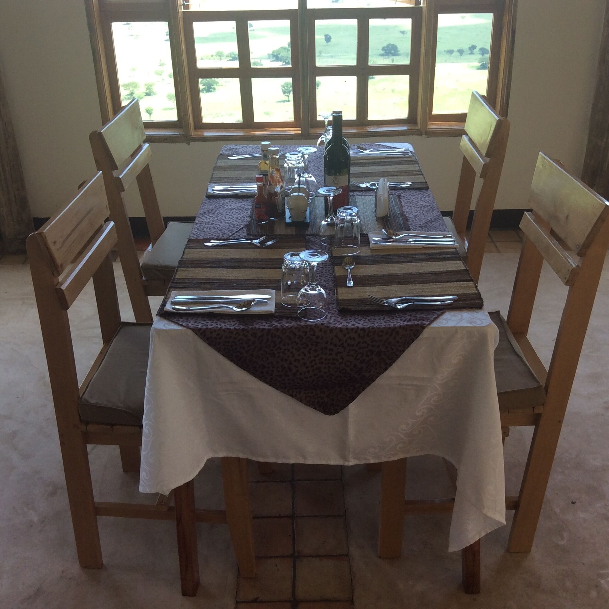 A dining table set for four with a view of a green landscape through a window.