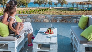 Un patio con un muro in pietra, un tavolo bianco con anguria e posate, e sedute con cuscini verdi.