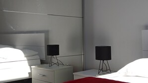 A modern bedroom with a bed, two bedside tables, a red blanket, and a large mirror.