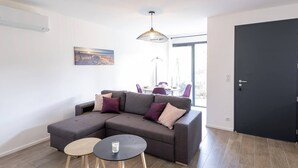 A modern living room with a sectional sofa, two small round tables, and a dining area with chairs. - Villa Renajolo. 6 pers, 3 min plage en voiture (STE LUCIE DE PORTO VECCHIO)