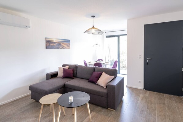 Una sala de estar moderna con un sofá modular, dos mesitas redondas y un comedor con sillas.