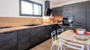 A modern kitchen with dark cabinets, a wooden countertop, a stainless steel sink, and a dining area with a table and chairs. - Villa Renajolo. 6 pers, 3 min plage en voiture (STE LUCIE DE PORTO VECCHIO)