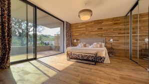 Een slaapkamer met een groot bed, houten vloeren, uitzicht door een schuifdeur en een plafondlamp.
