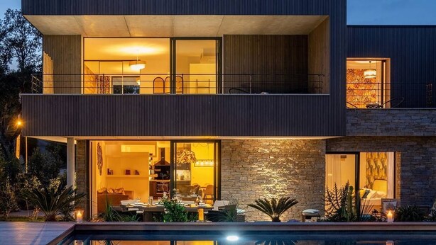 Een modern huis met twee verdiepingen, een zwembad, grote ramen en een gevel van natuursteen.