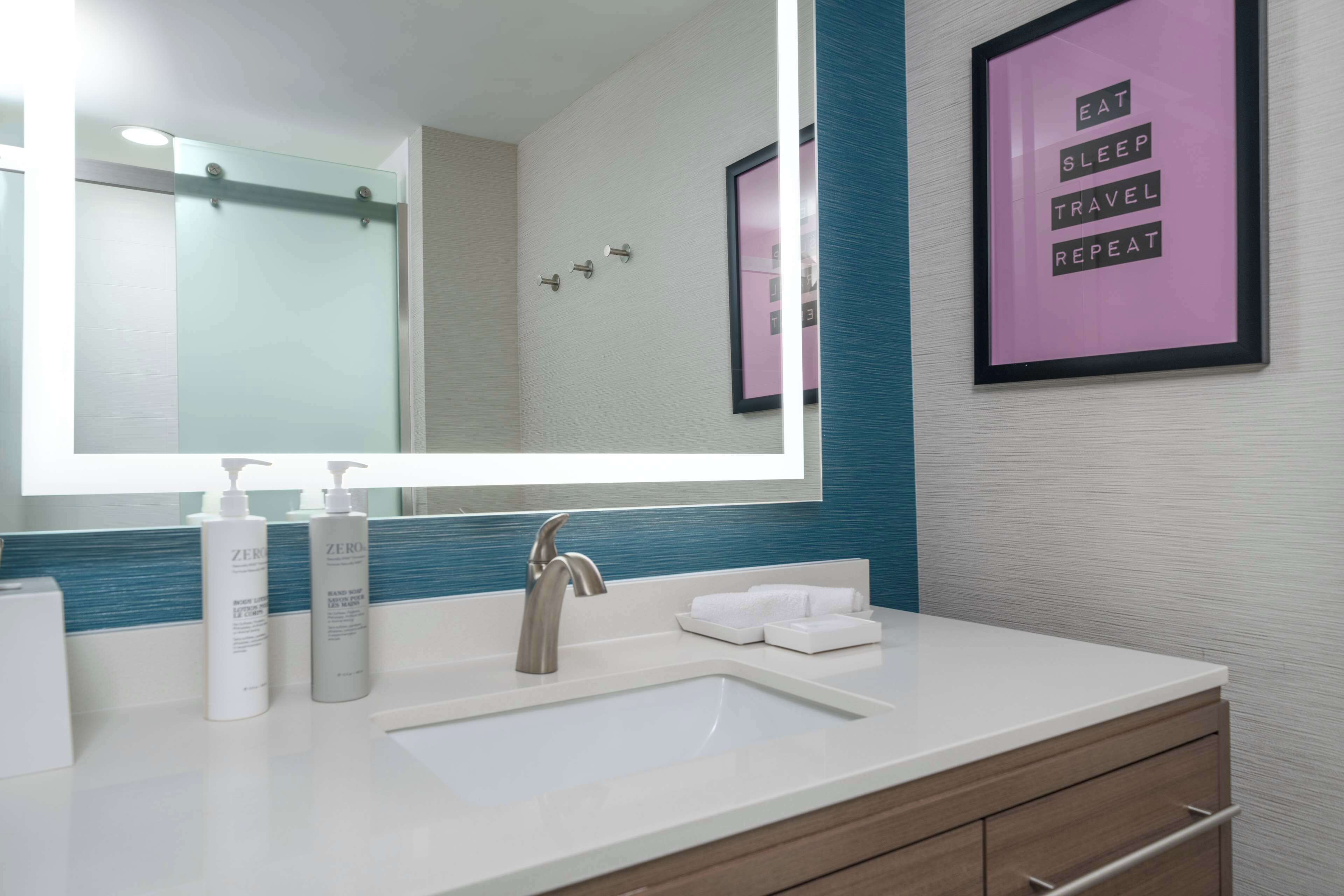 Un baño moderno con un espejo grande, un lavamanos y una cita inspiradora enmarcada en la pared.