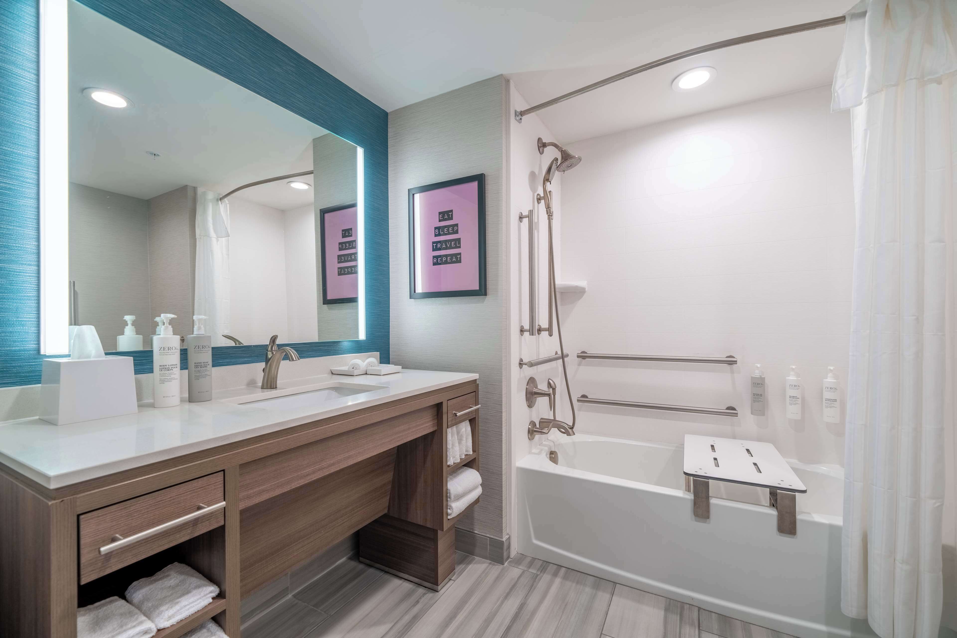 Un baño moderno con un espejo grande, dos lavamanos, una ducha con mampara de vidrio y una bañera con asiento para ducha.