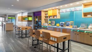 A modern restaurant with a long counter, multiple seating areas, and a variety of food and drink dispensers. - Home2 Suites by Hilton Fredericksburg South (Fredericksburg)
