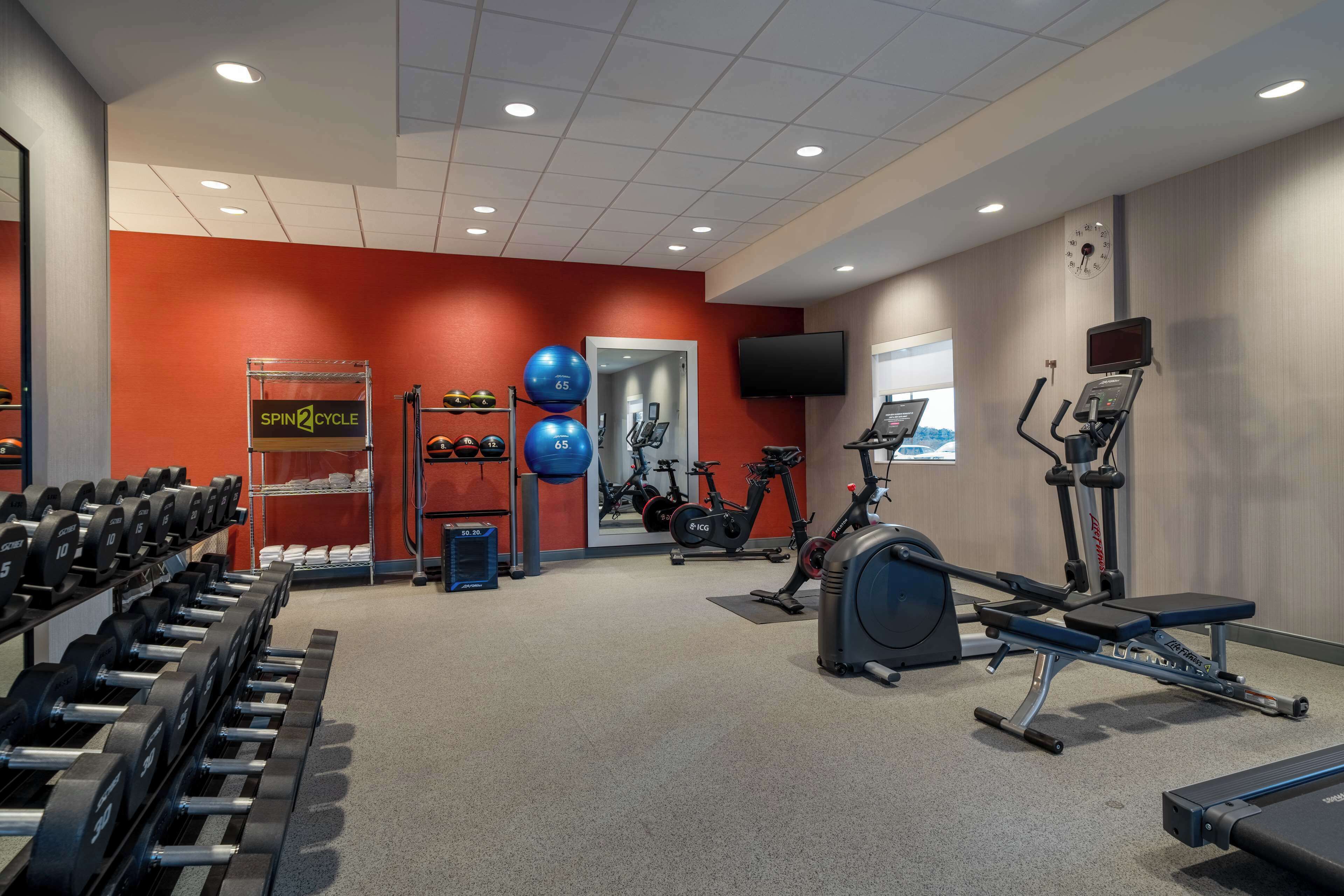Un gimnasio con equipamiento para levantamiento de pesas, máquinas de cardio y un reloj de pared.