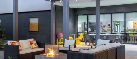 An outdoor seating area with wicker furniture, a fire pit, and a modern kitchen in the background.