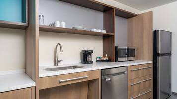 A modern kitchen with a stainless steel refrigerator, a built-in microwave, a coffee maker, and wooden cabinetry.