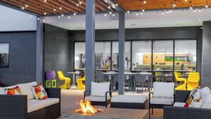 An outdoor seating area with wicker furniture, a fire pit, and a view of the kitchen area. - Home2 Suites by Hilton Fredericksburg South (Fredericksburg)