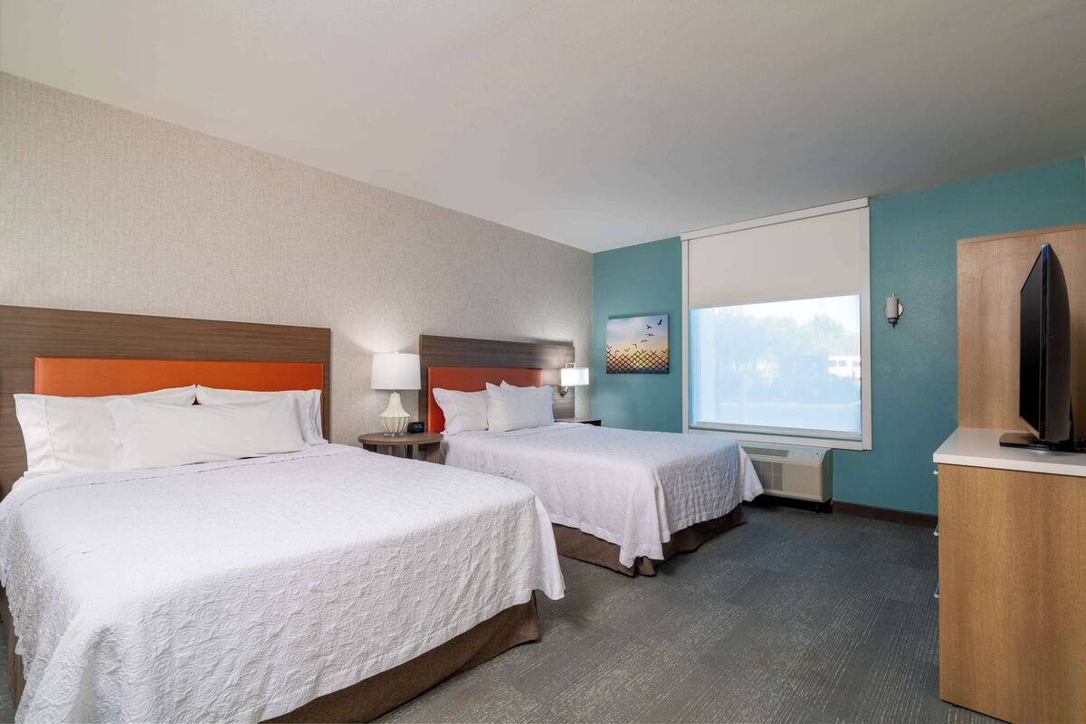 A hotel room with two beds, a television, a desk, and a window.