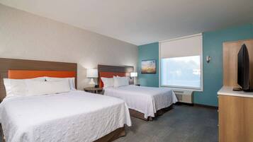 A hotel room with two beds, a television, a desk, and a window.