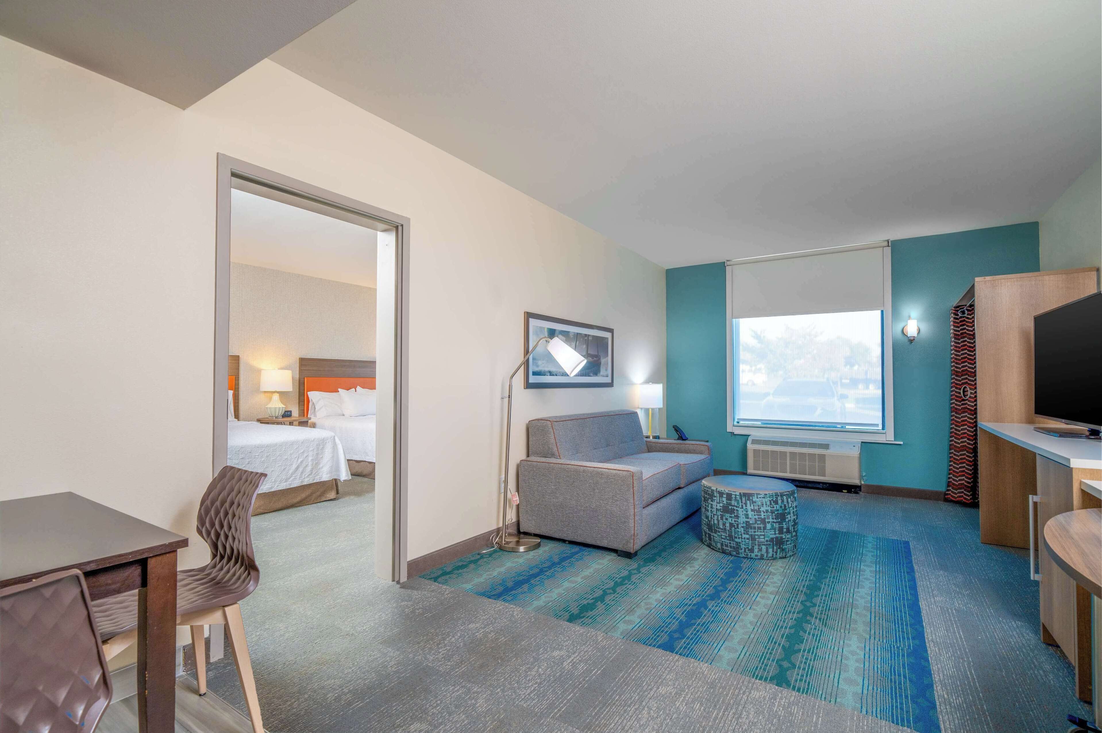 A hotel room with a bed, a sofa, a desk, a chair, a TV, and a window with a view.