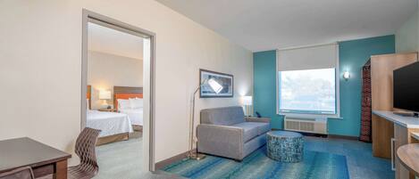 A hotel room with a bed, a sofa, a desk, a chair, a TV, and a window with a view.