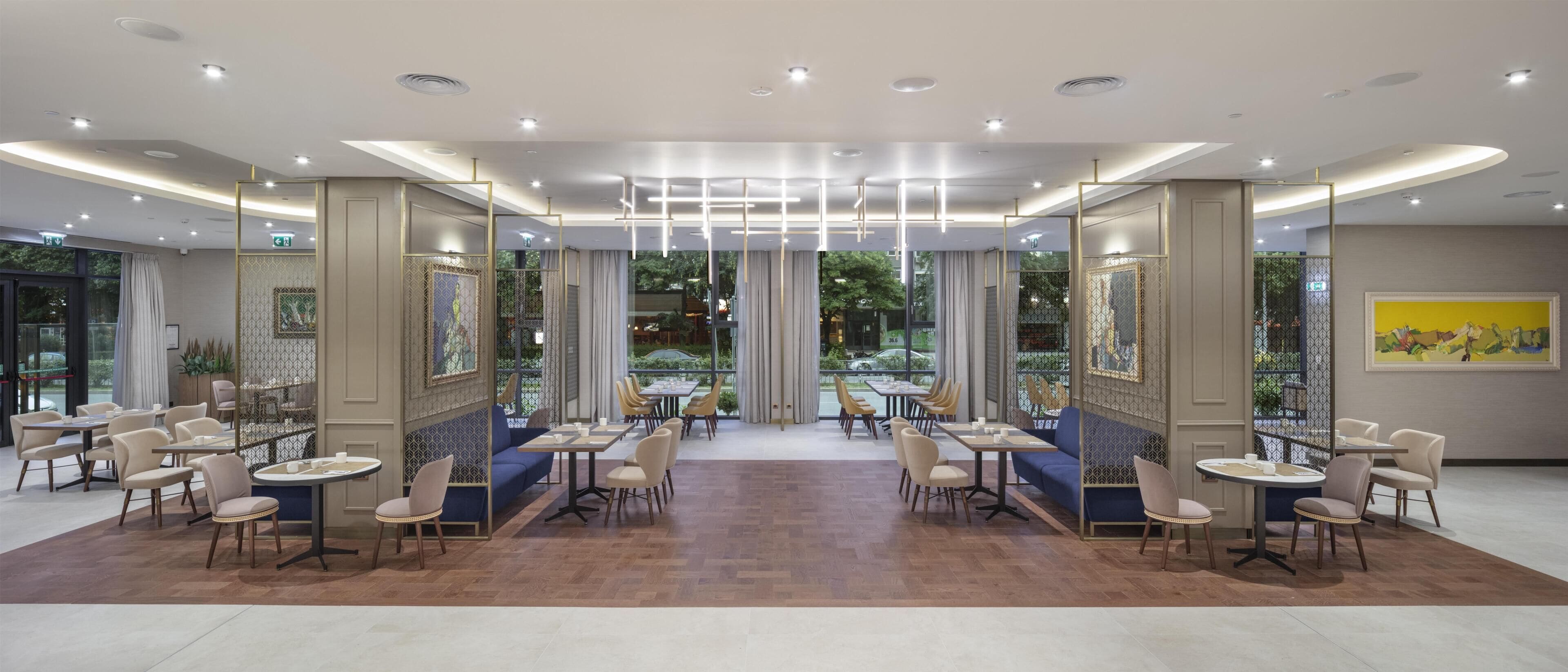 A modern dining area with round tables and chairs, a patterned floor, and a view of greenery outside.