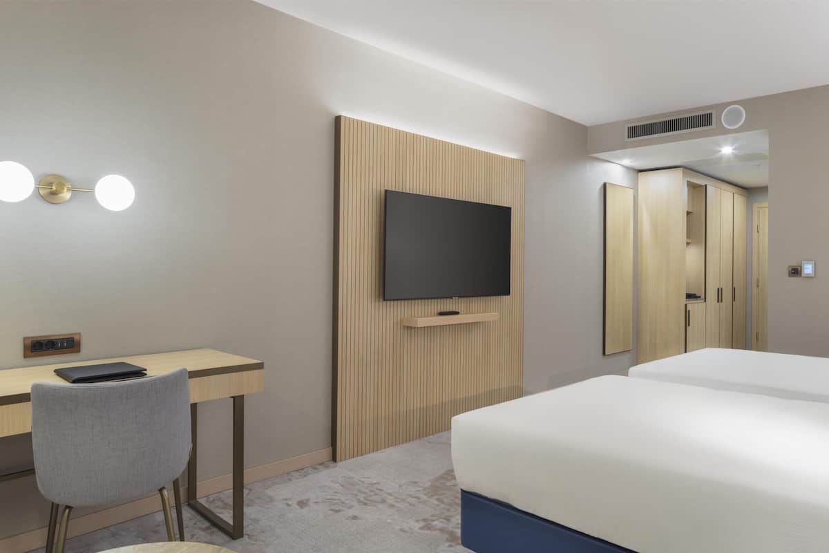 A hotel room with a bed, a desk, a chair, a television, and a wardrobe.