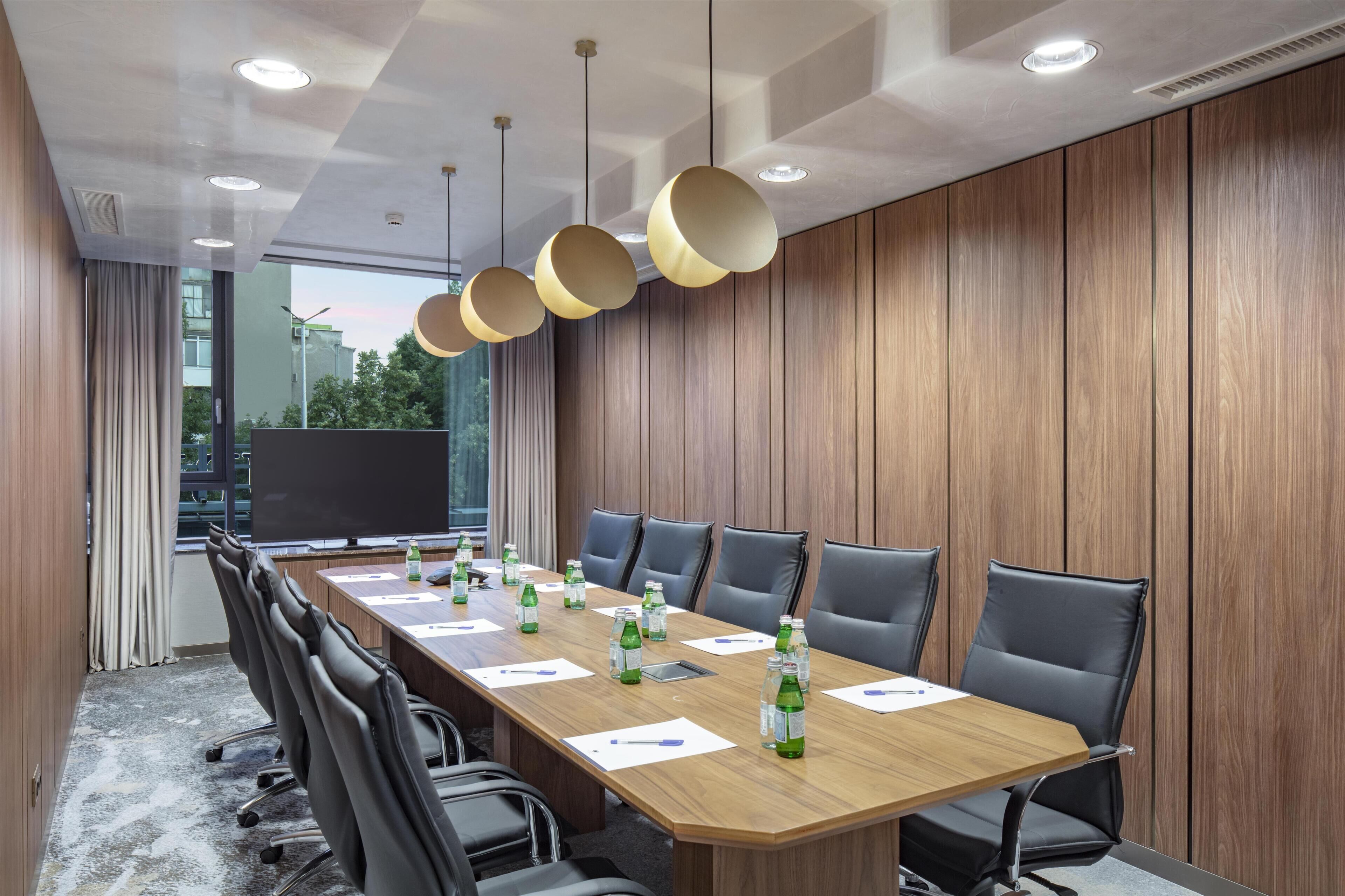 A conference room with a long table, black chairs, and hanging pendant lights.