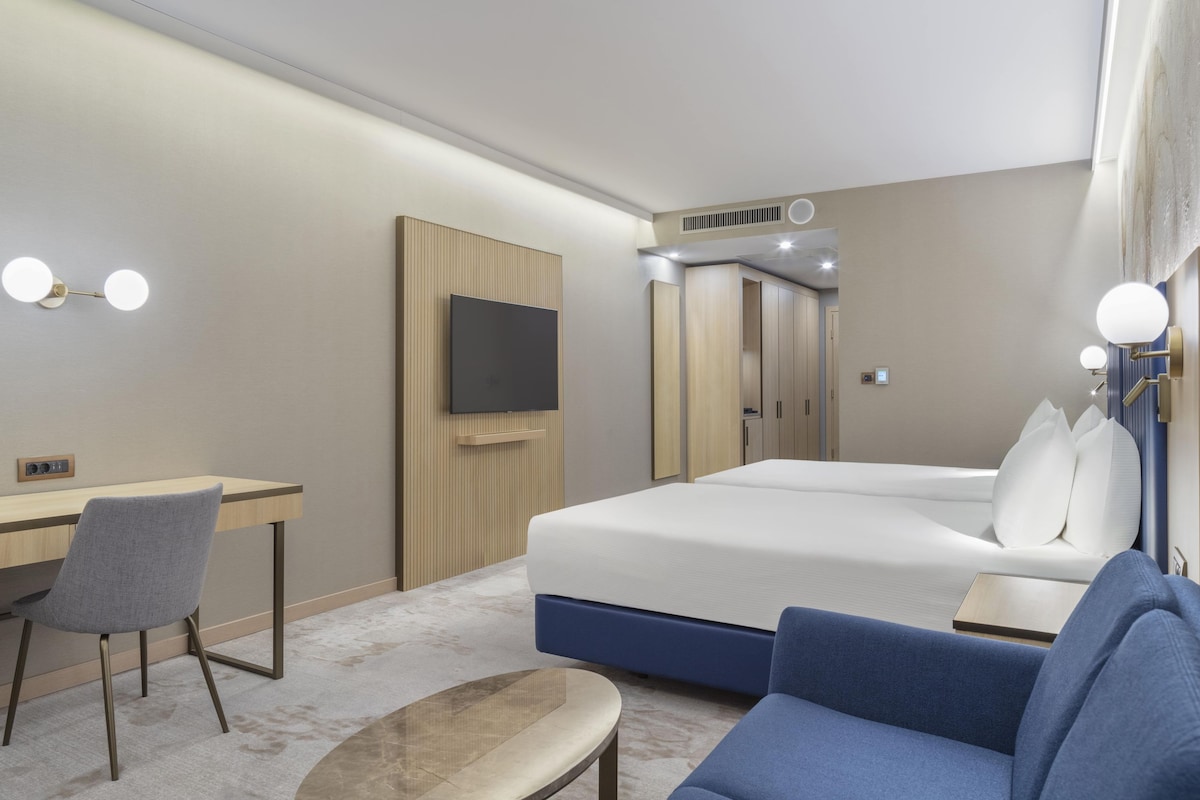 A hotel room with a bed, a desk, a chair, a TV, and a sofa.