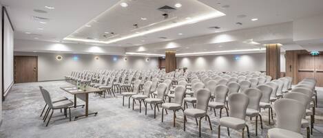 Un amplio salón de conferencias con filas de sillas, mesas y suelo alfombrado.