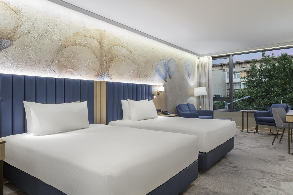 A hotel room with two beds, a desk, and a chair.