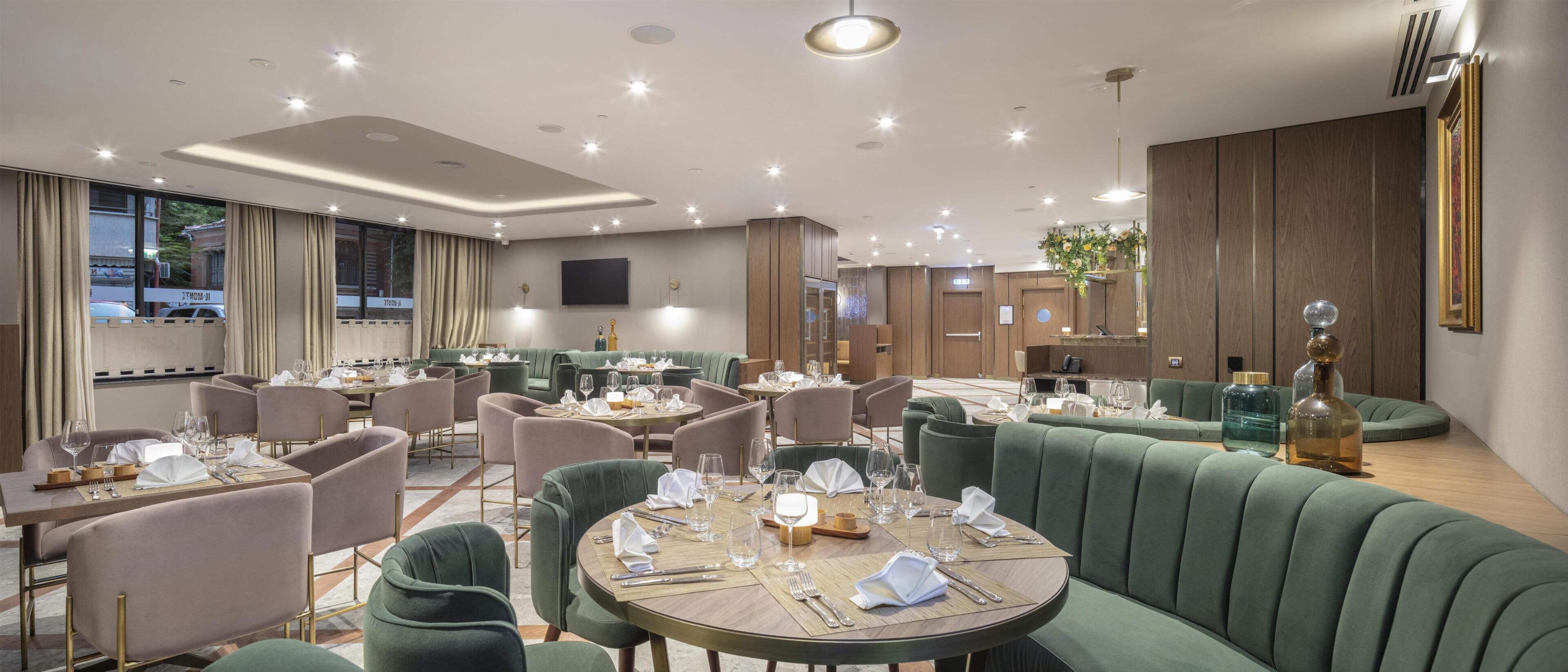 A modern restaurant with round tables, green upholstered seating, and a large mirror.