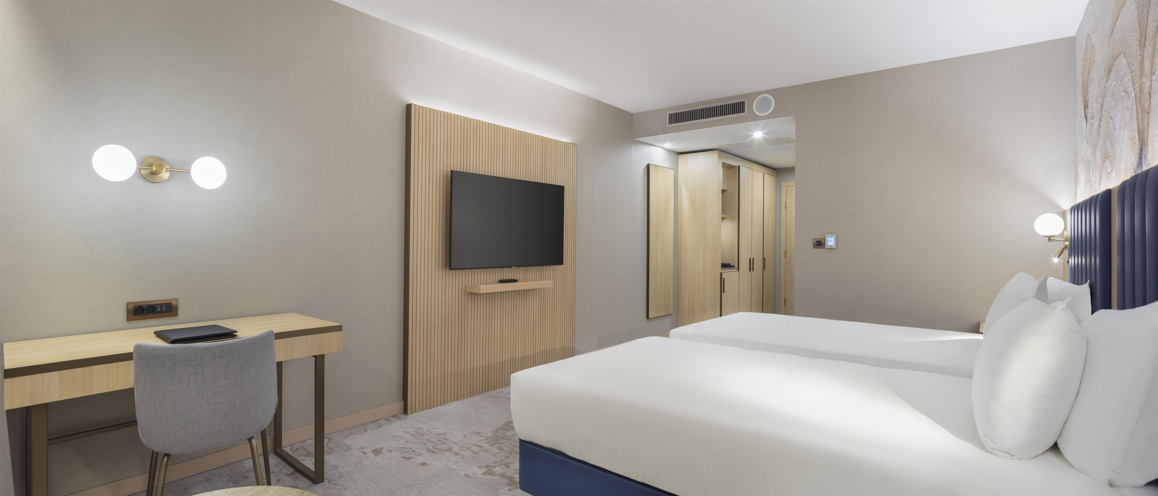 Quarto de hotel com escrivaninha, duas camas, televisão e guarda-roupa.