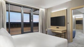 A hotel room with a bed, a desk, a television, and a sliding glass door to a balcony.