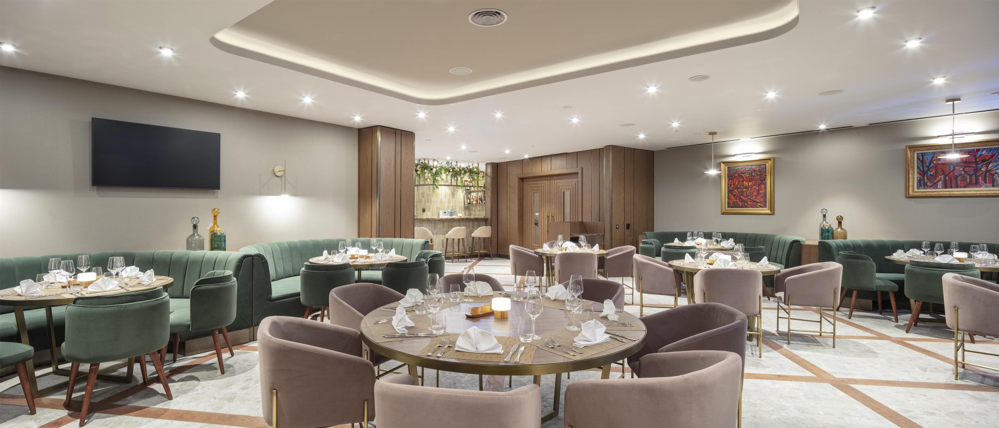 Un restaurante con mesas redondas, asientos tapizados en verde y un diseño de techo moderno.