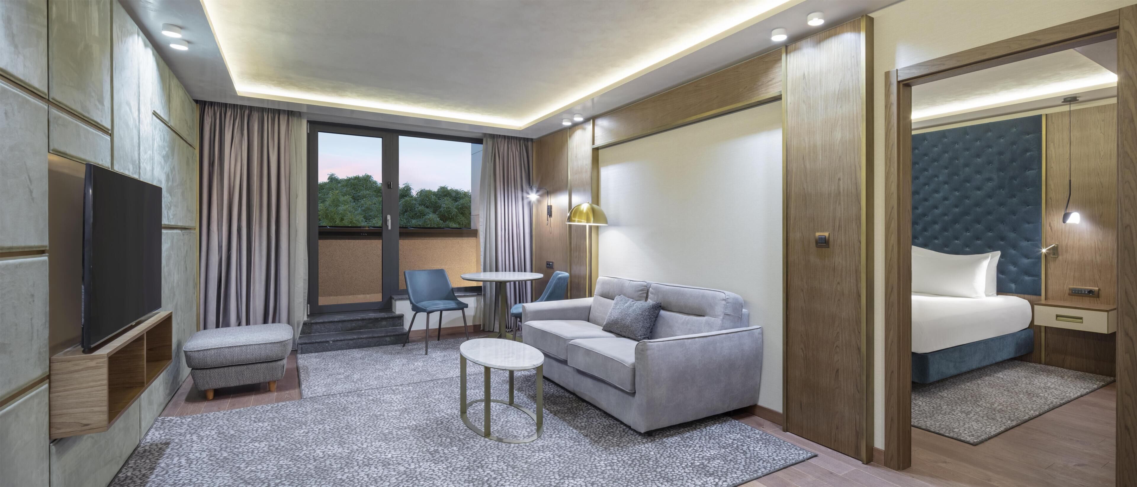 A modern hotel room with a sofa, a small table, a TV, and a bed.