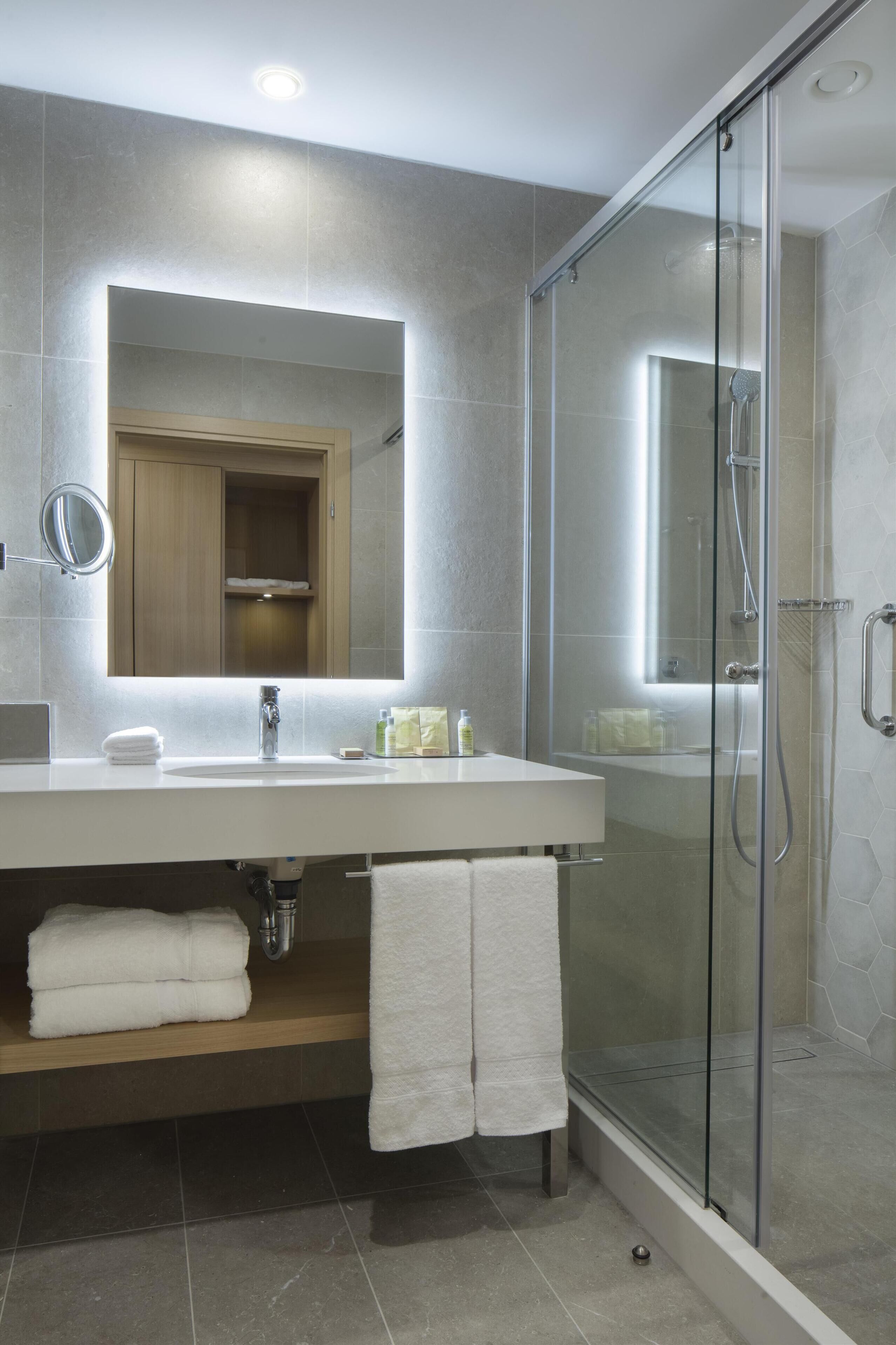 A modern bathroom with a glass-enclosed shower, a large mirror, and a built-in cabinet.