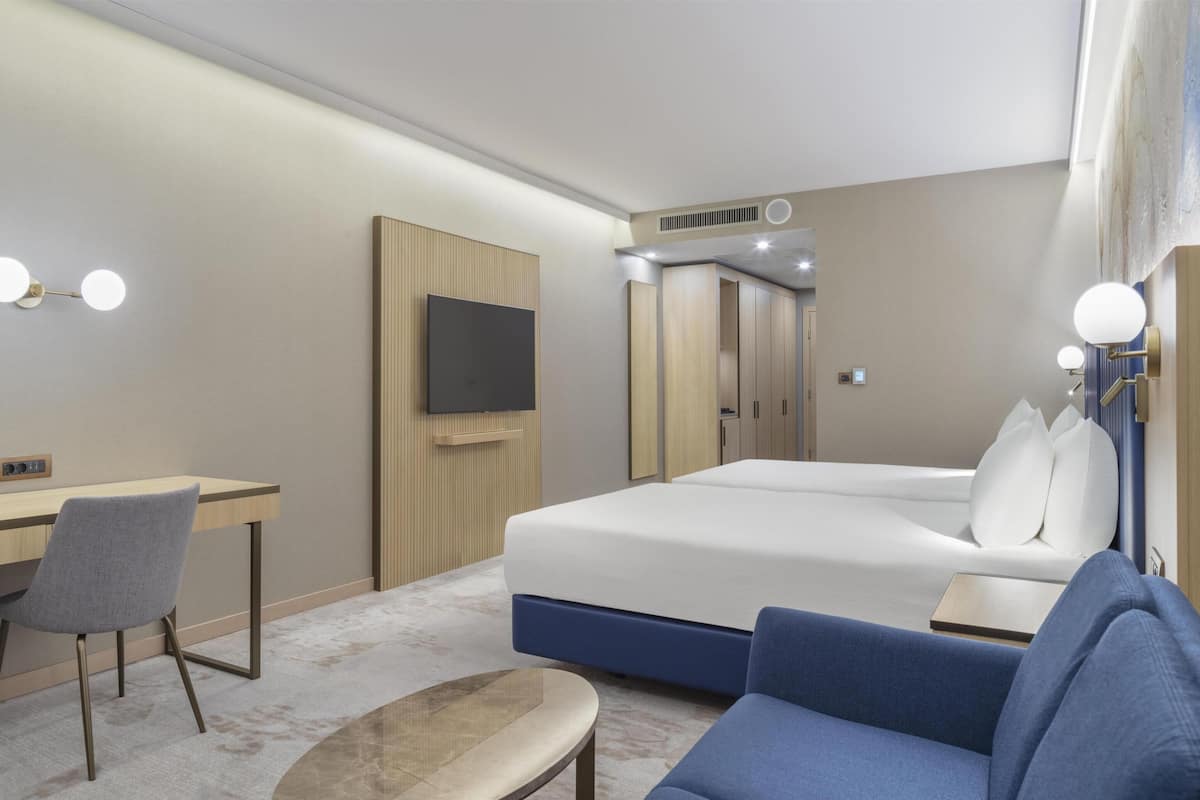 A hotel room with a bed, a desk, a chair, a TV, and a sofa.