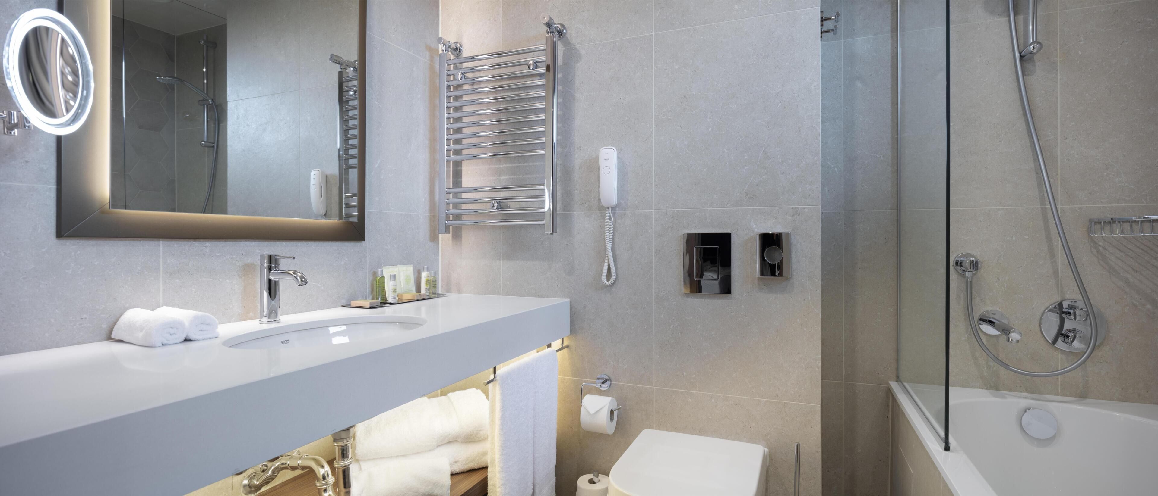 Un baño moderno con lavamanos, espejo, toallero, ducha e inodoro.