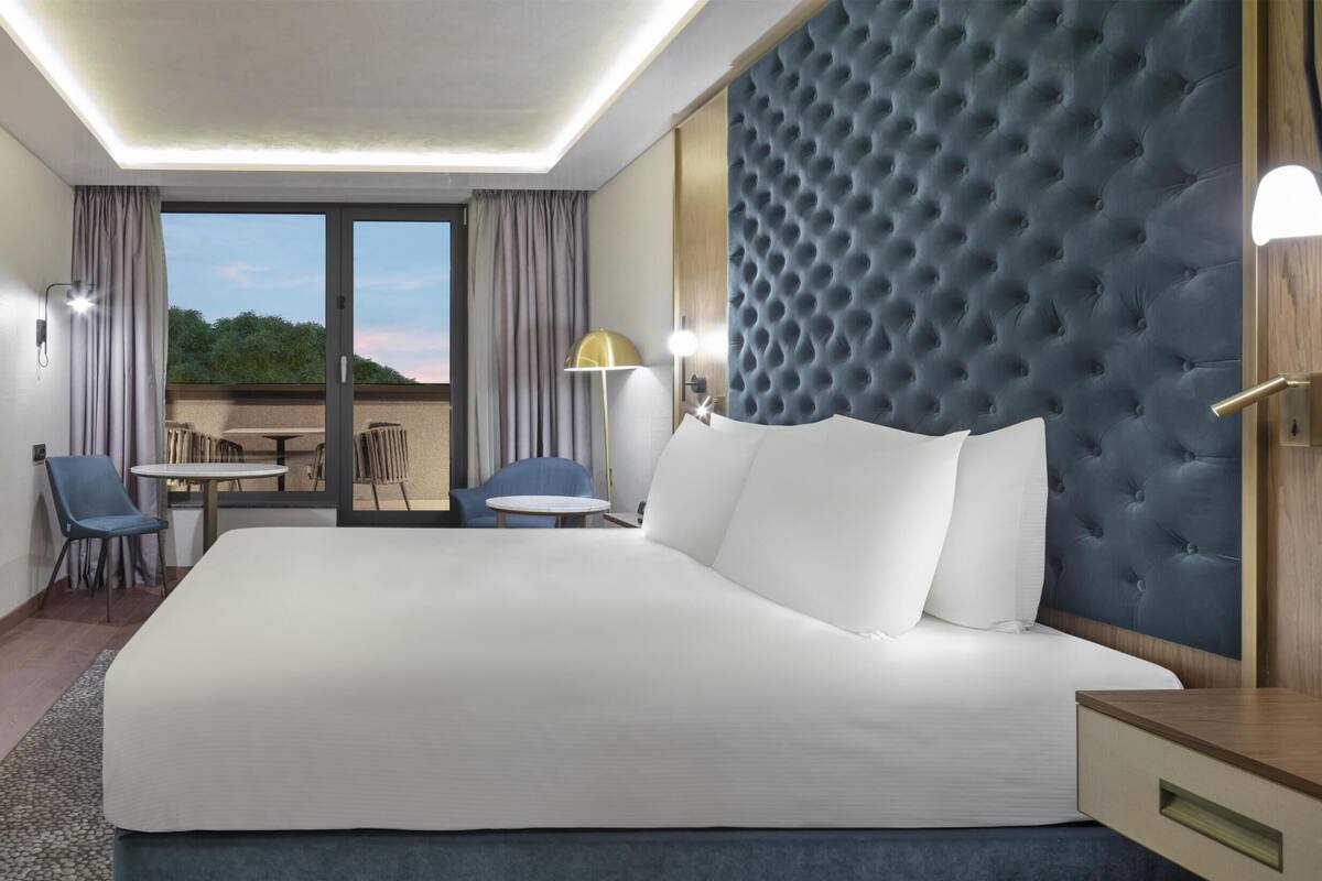 A hotel room with a large bed, a desk, two chairs, a TV, and a view of the outdoors.