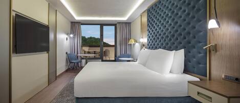 Habitación de hotel con una cama grande, un escritorio, dos sillas, un televisor y vistas al exterior.