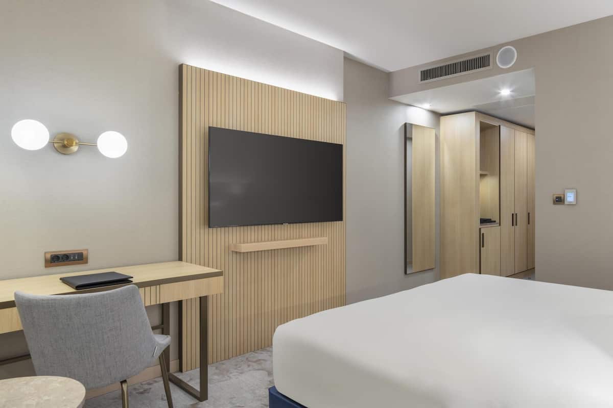 A hotel room with a bed, a desk with a chair, a television, and a wardrobe.