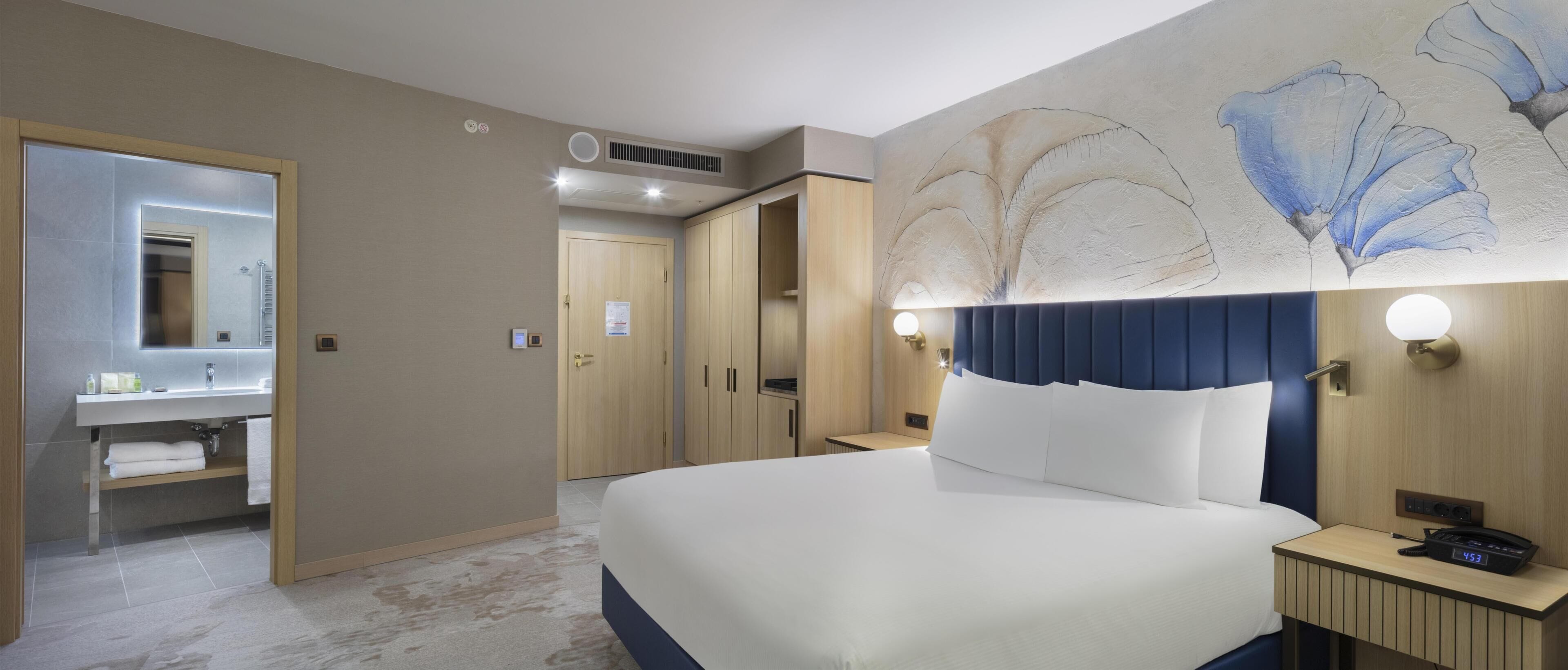 A hotel room with a bed, a bathroom with a mirror, and a door leading to another room.