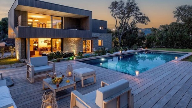 Et moderne hus i to etager med swimmingpool, udendørs møbler og et godt oplyst interiør.