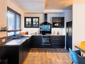 A modern kitchen with black cabinetry, a central island, a built-in oven, and a window with blinds.