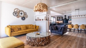 En moderne stue med en gul sofa, et rundt sofabord og et spiseområde med stole.