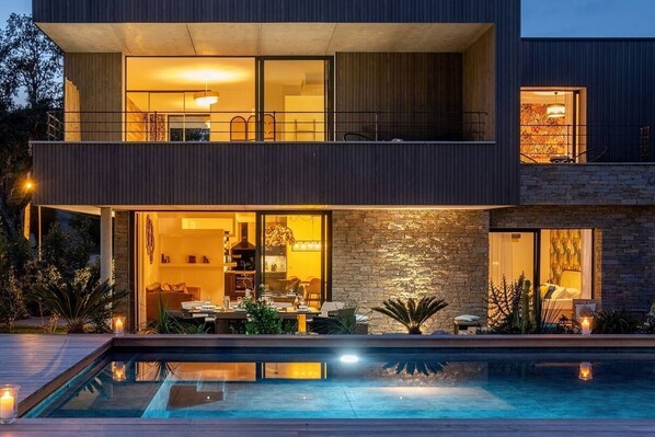A modern two-story house with a swimming pool, large windows, and a stone facade.