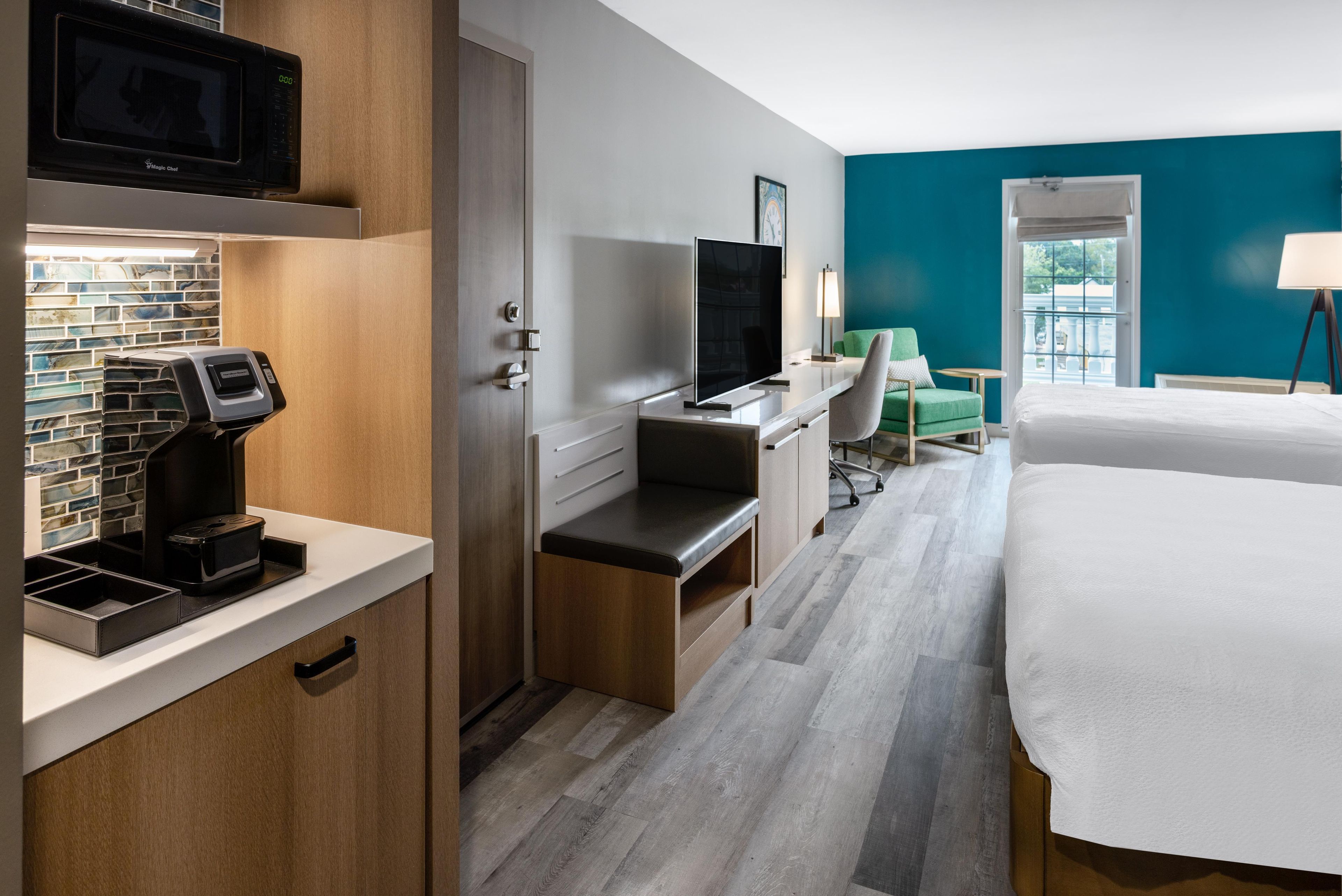 A hotel room with a bed, desk, chair, TV, and a view of the outdoors.