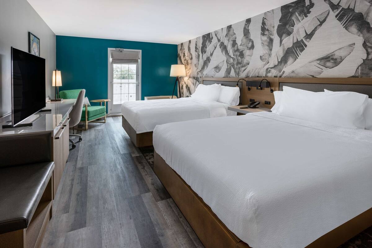 A hotel room with two beds, a desk with a TV, a chair, and a large window.