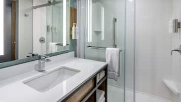 A modern bathroom with a large mirror, a white sink, and a glass-enclosed shower area.