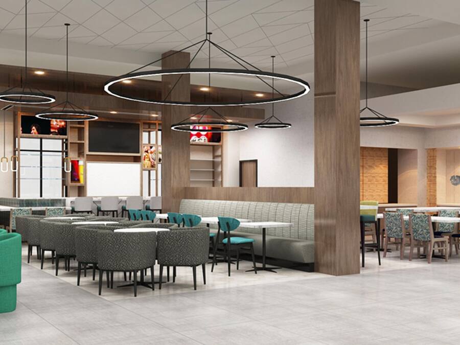 A modern restaurant interior with high ceilings, pendant lighting, and a mix of seating arrangements including booths and tables.